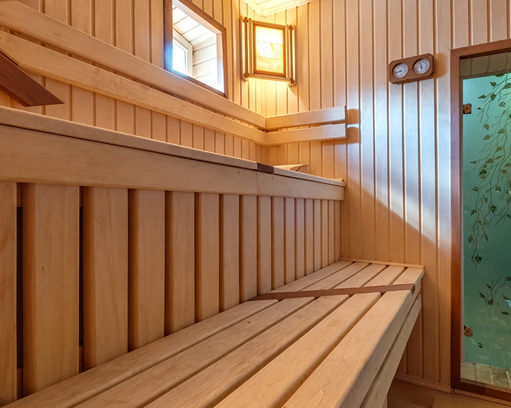 Nyrenoverad bastu med ljust trä, flernivåbänkar och en dekorativ frostglassdörr med lövmönster – badrumsrenovering utförd av Grand Construction Stockholm.