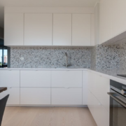 Modernt renoverat kök med vita handtagslösa luckor, terrazzobänkskiva och stänkskydd i granit samt inbyggda vitvaror – köksbyte i Stockholm utfört av Grand Construction.