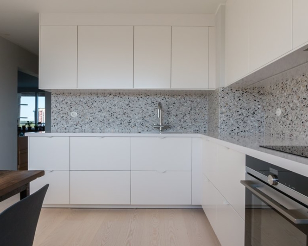 Modernt renoverat kök med vita handtagslösa luckor, terrazzobänkskiva och stänkskydd i granit samt inbyggda vitvaror – köksbyte i Stockholm utfört av Grand Construction.