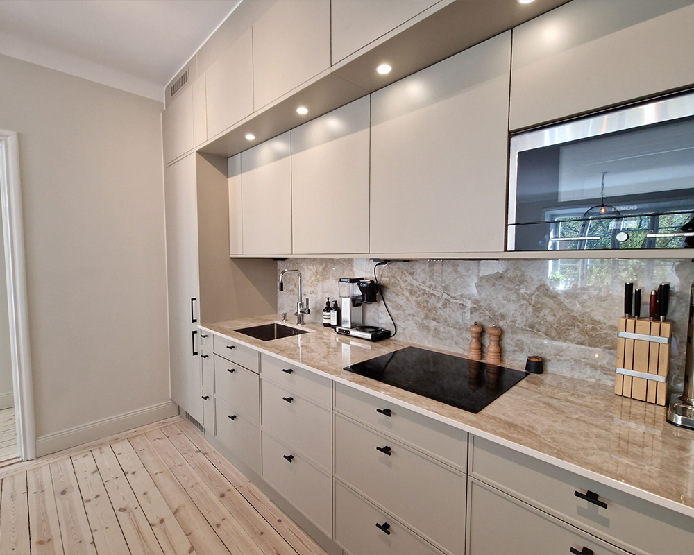 Köksrenovering i Stockholm med beigebeige luckor, marmorbänkskiva och stänkskydd i natursten – utfört av Grand Construction