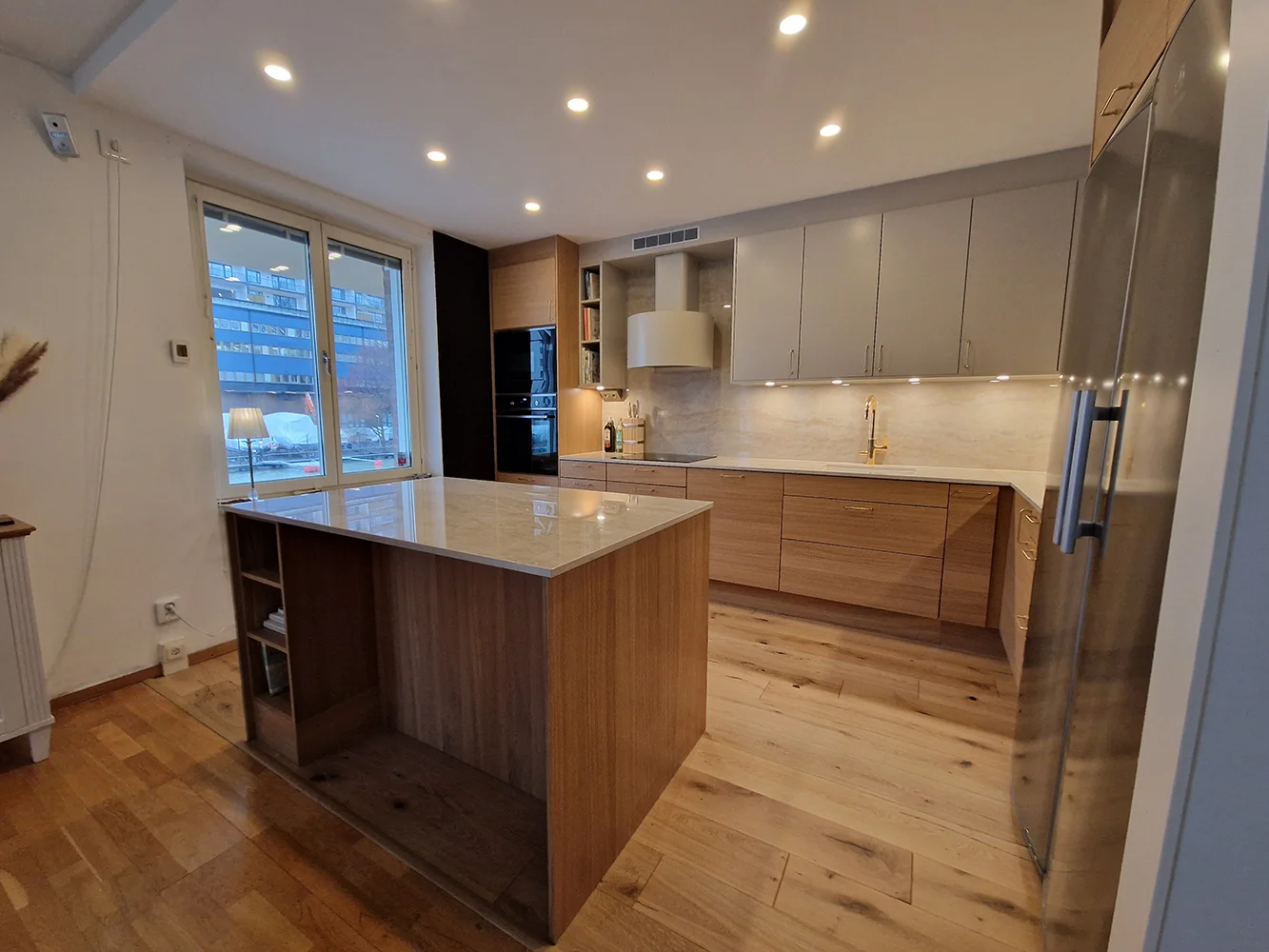 Köksrenovering i Stockholm med valnötsfanerade luckor, marmorbänkskiva, gulddetaljer och inbyggda ugnar – utfört av Grand Construction